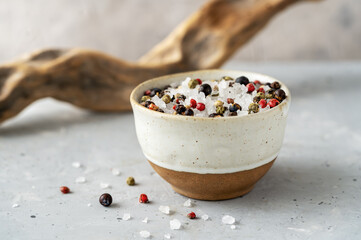 Sea salt with mix peppercorns spices in small bowl on concrete background, wooden branch or snag...