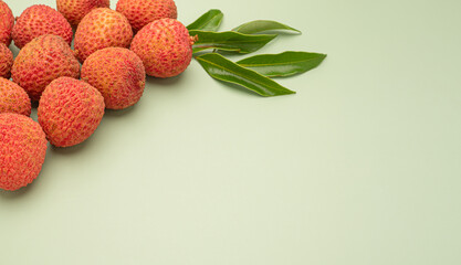 A pile of fresh ripe lychees fruit with green leaves on a green background.