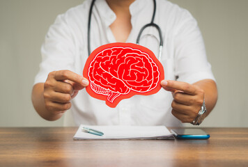 Brain Health and dementia. Physician holding a red brain symbol while sitting at the table in the hospital.