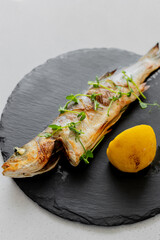 Grilled seabass served on slate plate with lemon and micro green