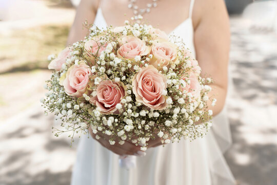 A girl in a white dress holds a wedding bouquet of roses and gypsophila in her hands close-up.