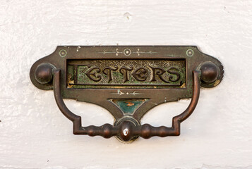 Ornate brass door knocker and mail slot in a white door