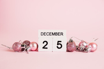Christmas, wooden calendar with date December 25 and Christmas tree decorations on pink background. Christmas and New Year celebration concept.