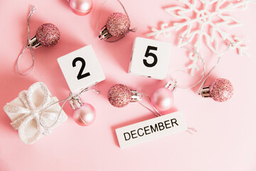Flatlay, Christmas, wooden calendar with date December 25 and Christmas tree decorations on pink background. Christmas and New Year celebration concept.
