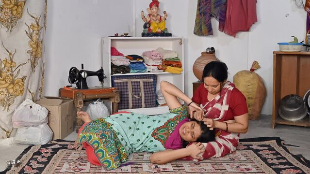 A young teenage girl is scratching her head while lying down on her mother's lap - infection  itchy  poor hygiene . A caring village mother is checking for lice / nits in her teenage daughter's hai...