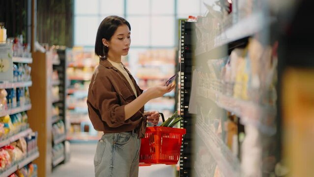 Woman picks up product from shelf holding shopping basket