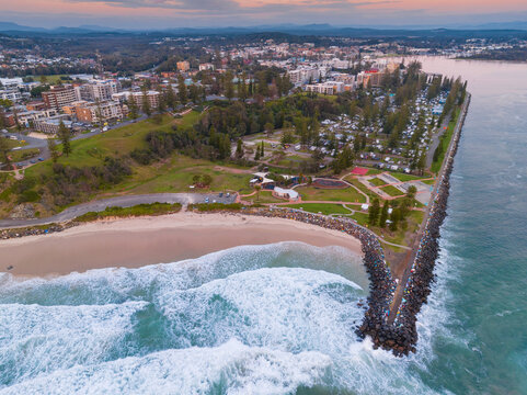 Aerial view of waves breaking on a beach in front of a reserve with a skate park and walking tracks