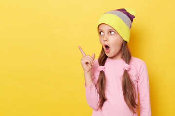 Shocked astonished little girl with ponytails wearing pink shirt and beanie hat posing isolated...