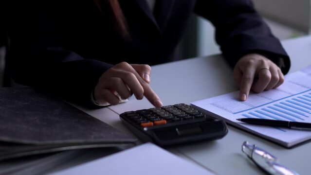 Young Asian businesswoman using a calculator to for doing  finance report working at office desk.