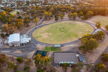 Aerial view of a dry sports oval and buildings surrounded by gum trees