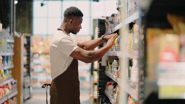 African American worker arranges goods on market shelf
