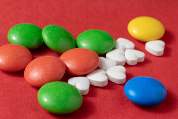Close-up of a handful of heart-shaped pills and colored dragees on a red background.