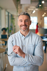 Portrait Of Smiling Mature Businessman Holding Glasses  Standing In Busy Office 