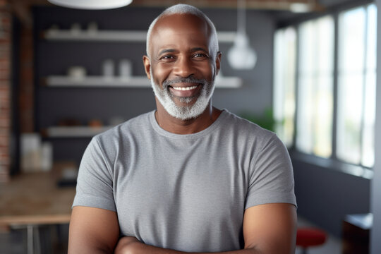 Confident mature man with a beard stands at home, smiling, arms crossed. Happy African senior exudes positivity while looking at the camera.