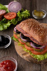 photo of a fresh food sandwich on a wooden board. sausage, onions, black olives, fresh lettuce leaf, bread
