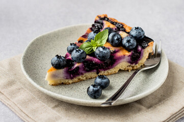a plate with a piece of blueberry pie, in the background berries in a bowl, on a light.