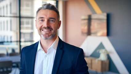 Portrait Of Smiling Mature Businessman Standing In Empty Office 