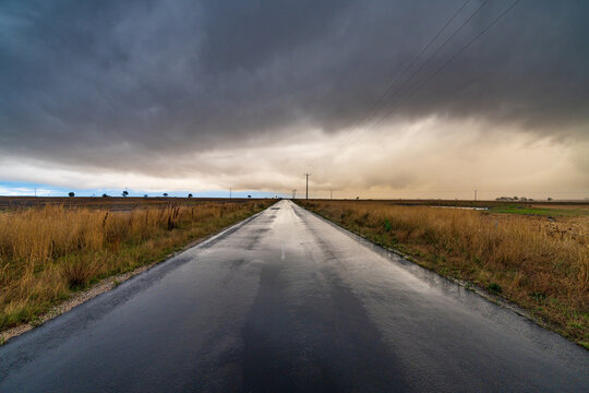 Wide angled view down a country road with bright gap under dark storm clouds