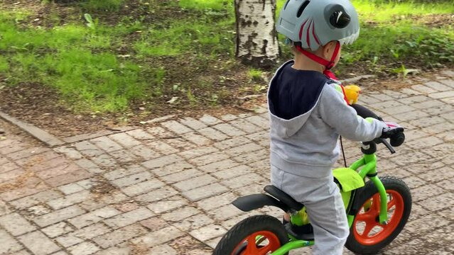 toddler child in protective helmet riding balance bike in summer park