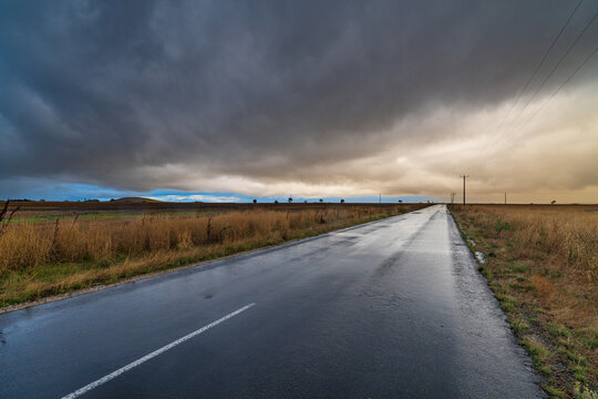 Wide angled view down a country road with bright gap under dark storm clouds