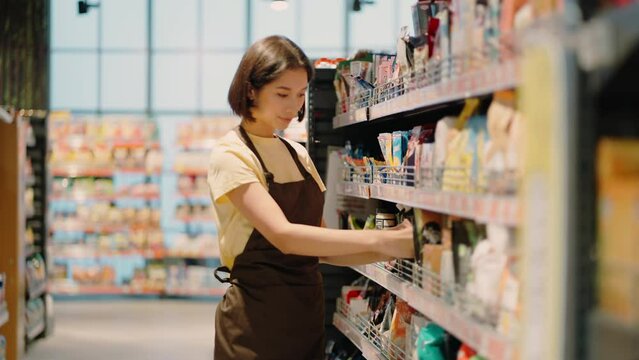 Woman supermarket employee arranges goods on shelf