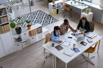 Wide angle top view of business team working together at meeting table in office and pointing at documents with data charts, copy space