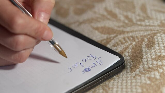 Closeup female Caucasian hand writing words in Spanish on white paper. Close-up unrecognizable woman handwriting amor dolor murir meaning love pain death