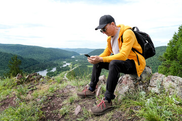 man with backpack have a rest during hiking mountains. Tourist drink water and relax, sitting rock at the top of hill.
