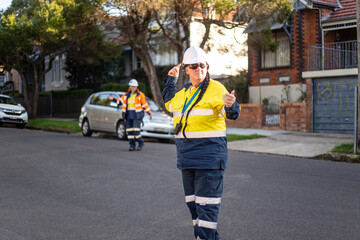 Woman road worker with white helmet and yellow jacket standing on the road directing traffic