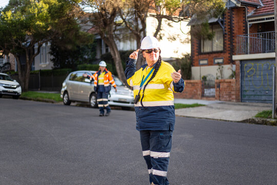 Woman road worker with white helmet and yellow jacket standing on the road directing traffic
