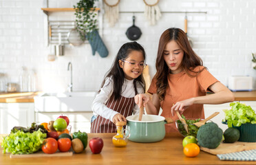 Portrait of enjoy happy love asian family mother with little asian girl daughter child help cooking food healthy eat with fresh vegetable testing smell soup in a pot with spoon.helping mommy  - obrazy, fototapety, plakaty