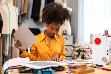 Portrait of young african american woman fashion designer stylish sitting and working with color samples.Attractive young african girl work with colorful fabrics at fashion studio