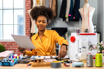 Portrait of young african american woman fashion designer stylish sitting and working with color samples.Attractive young african girl work with colorful fabrics at fashion studio