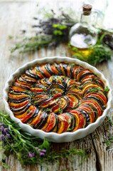 Traditional tian made of sliced vegetables in casserole dish on wooden table, focus on center part, close up view