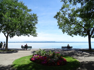 gente sentada y paseando relajada en un banco delante de el lago con monta&ntilde;as de fondo, en suiza