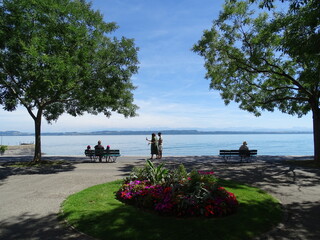 gente sentada y paseando relajada en un banco delante de el lago con monta&ntilde;as de fondo, en suiza