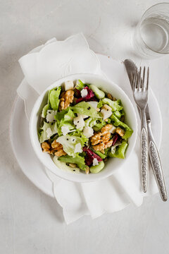 Green salad, with salad, parmesan cheese, walnuts and pistachios, sesame seeds on white table.