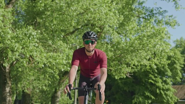 Portrait of caucasian man in helmet and sunglasses cycling light carbon road bike in outdoor wild space. Relaxed well-built athlete enjoying fresh air while performing moderate-intensity activity.