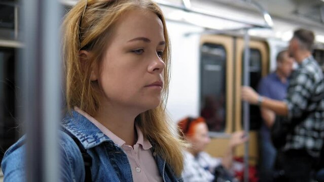 Close-up portrait of a young woman with a backpack in a subway car. A woman rides the subway to work in a crowded subway car.