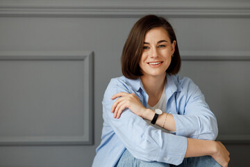 Portrait of a young beautiful girl which is looking at the camera and holding a hand with a watch...