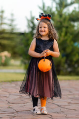 a cute little girl in a witch costume for Halloween walks in the park in a basket of candies in the form of a pumpkin