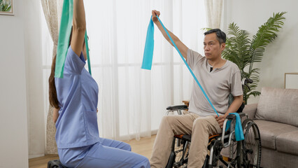 asian Japanese woman physiotherapy nursing aide assisting elderly man on wheelchair to use elastic band during rehabilitation exercise. they pull and stretch the tape upward