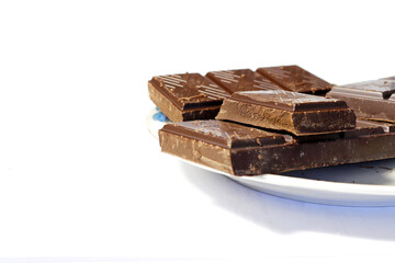 Close-up of a chocolate bar broken into pieces laid out on a saucer. Side view.