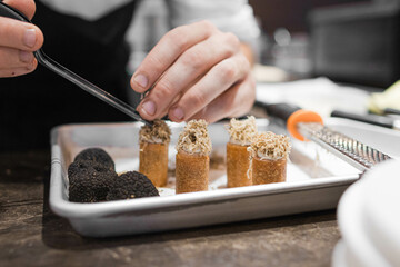 Photo of a chef's hands putting shredded truffle with tweezers on appetizers.
