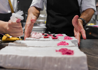 Photo of two chefs' hands working together and delivering a finished dish in a gastronomic...