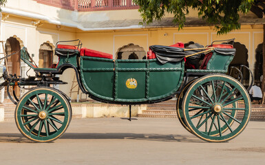 Side profile shot of a Rajputana Chariot painte green and yellow with unidentifiable man sitting under tree in background.