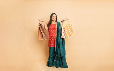 Portrait of young beautiful indian woman wearing traditional outfit holding shopping bags standing...