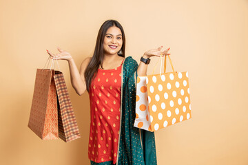 Cheerful young beautiful indian woman wearing traditional outfit holding shopping bags standing...