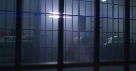 African American prisoner in orange uniform does push-ups and shadow boxing in prison cell. Inmate serves imprisonment term for crimes in jail. Criminal in detention center or correctional facility.