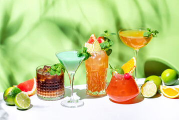 Alcoholic beverages, summer cocktail party. Multicolored low alcohol drink glasses set. Green background, hard light, shadow pattern